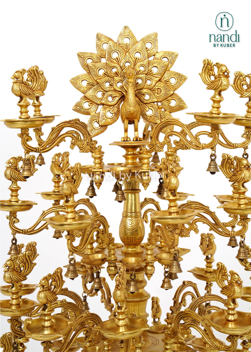 Large handcrafted brass Deepam with multiple oil lamp tiers, peacock motifs, floral detailing, and hanging bells for temples and pooja spaces.