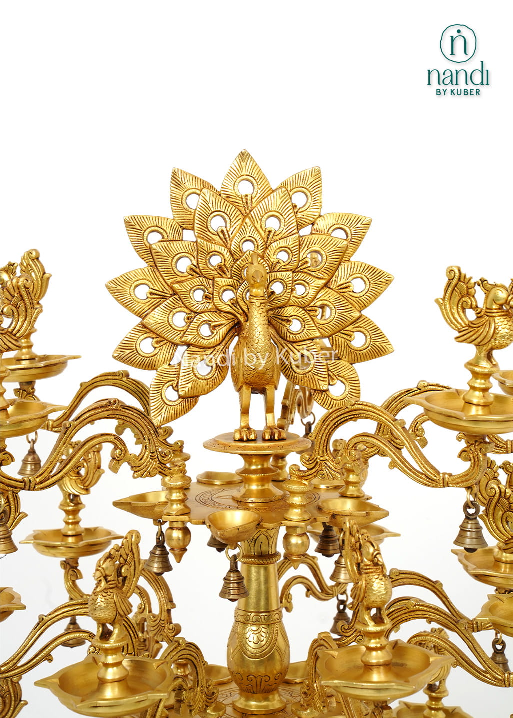 Large handcrafted brass Deepam with multiple oil lamp tiers, peacock motifs, floral detailing, and hanging bells for temples and pooja spaces.