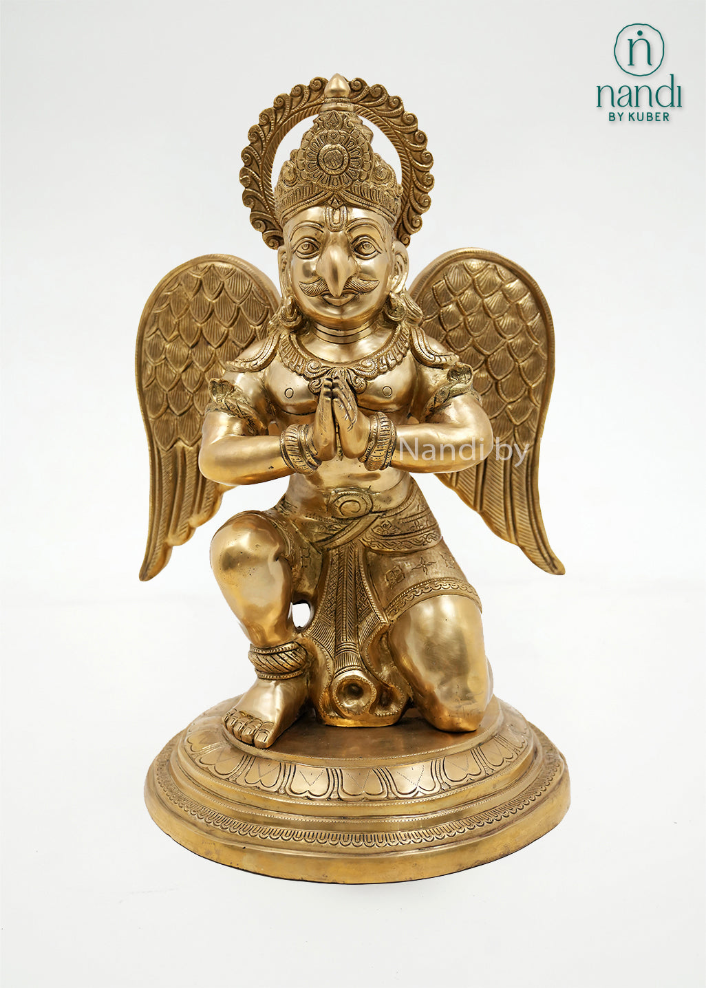 Handcrafted brass Garuda sitting statue with folded hands, detailed wings, ornate crown, and round pedestal, ideal for home temples, spiritual décor, and sacred spaces.