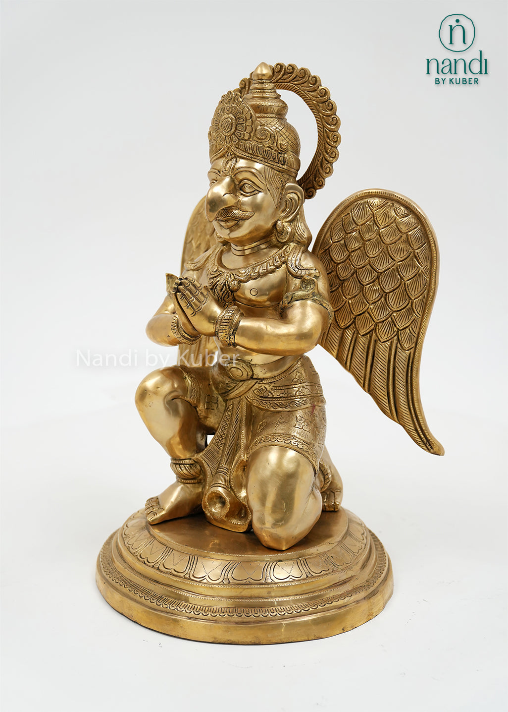 Handcrafted brass Garuda sitting statue with folded hands, detailed wings, ornate crown, and round pedestal, ideal for home temples, spiritual décor, and sacred spaces.