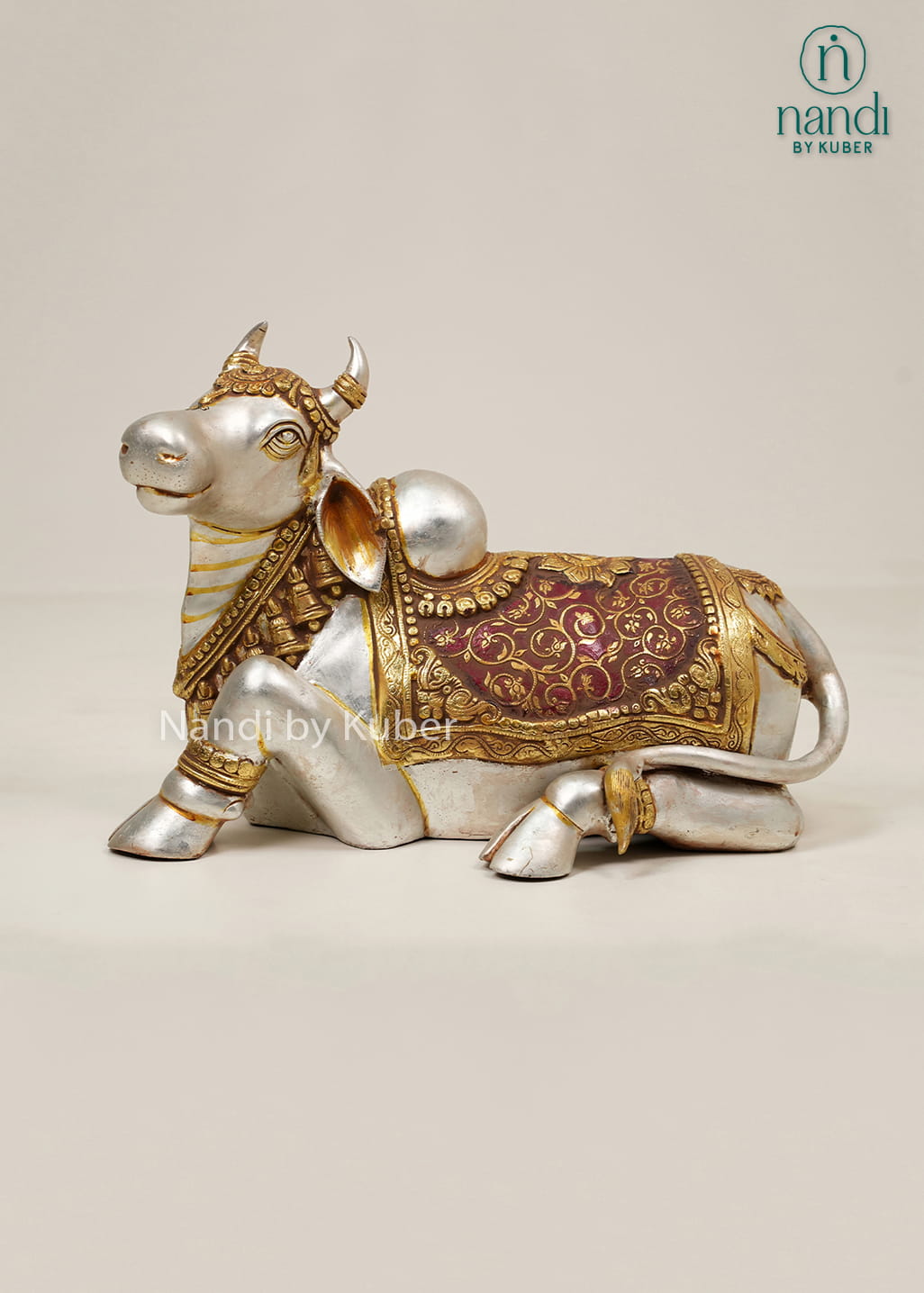Silver and gold-tone Nandi bull statue with ornate carvings, decorative saddle cloth, and traditional seated design.