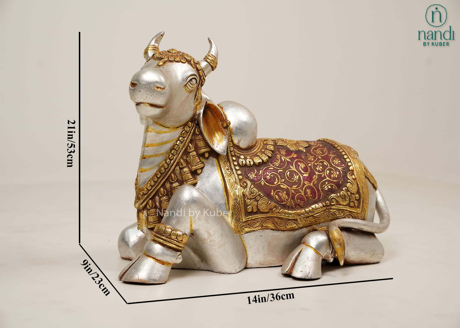 Silver and gold-tone Nandi bull statue with ornate carvings, decorative saddle cloth, and traditional seated design.