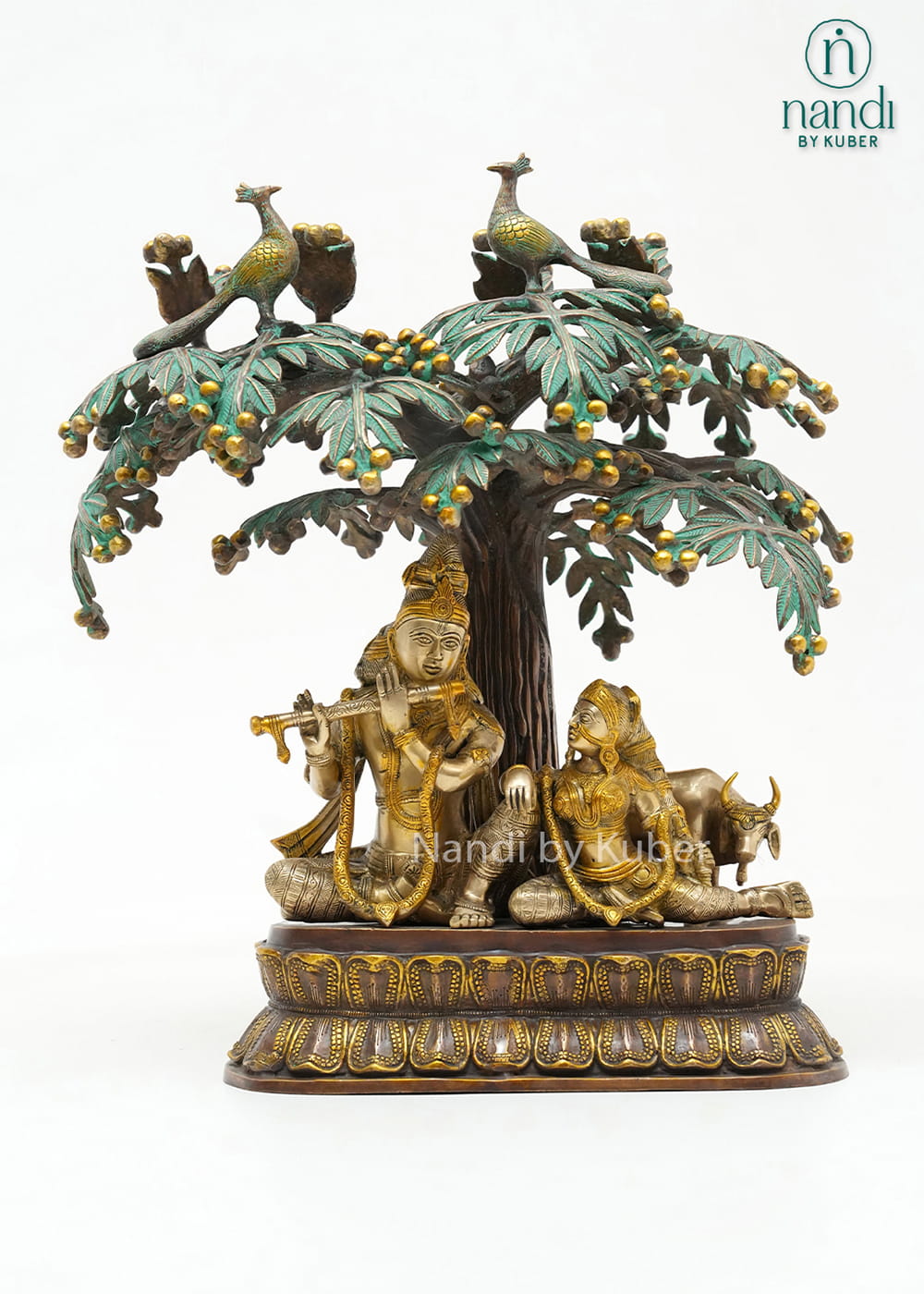 Decorative three-tone brass Radha Krishna statue beneath an ornate tree with peacocks, symbolizing love, devotion, and harmony.