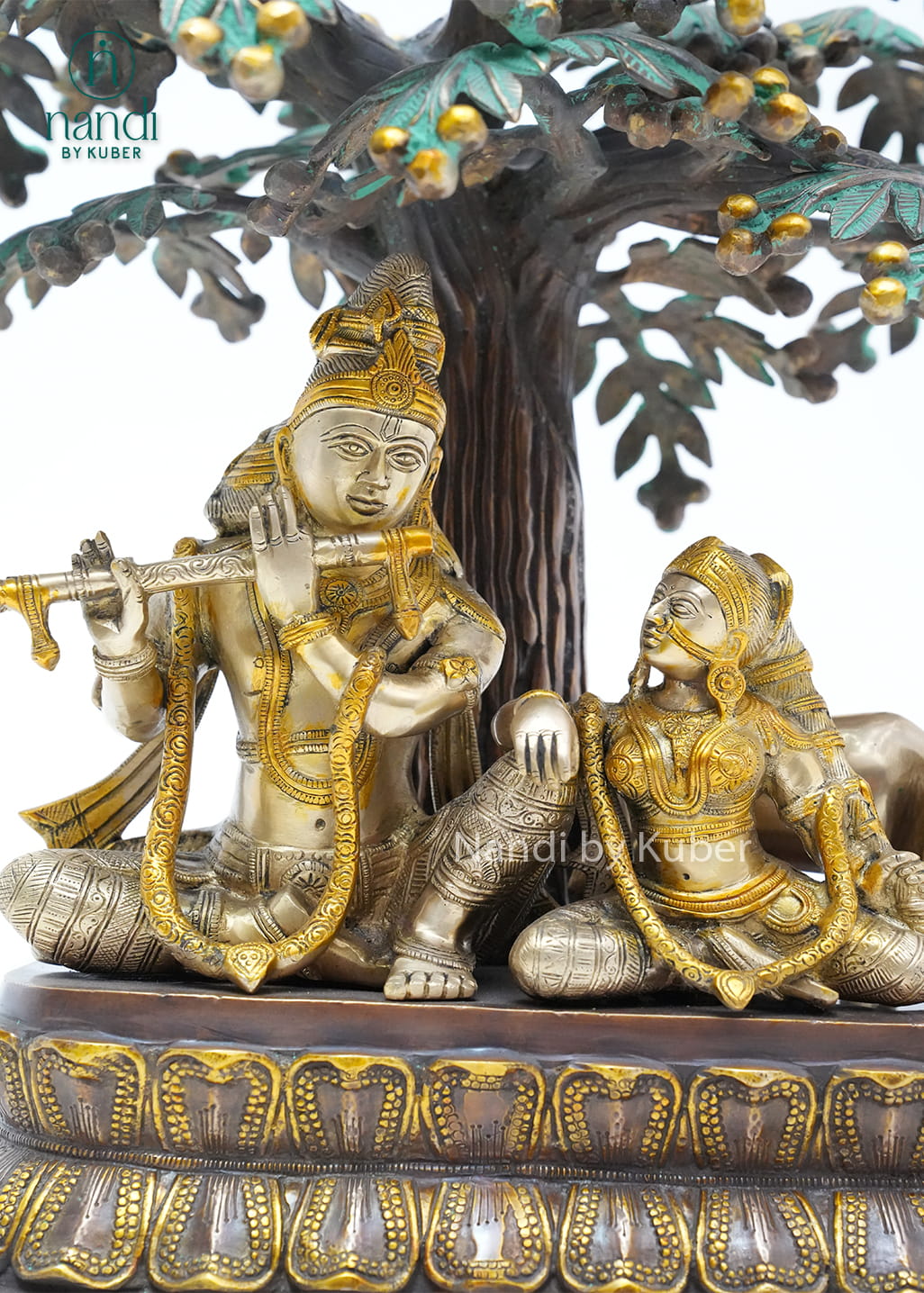 Decorative three-tone brass Radha Krishna statue beneath an ornate tree with peacocks, symbolizing love, devotion, and harmony.