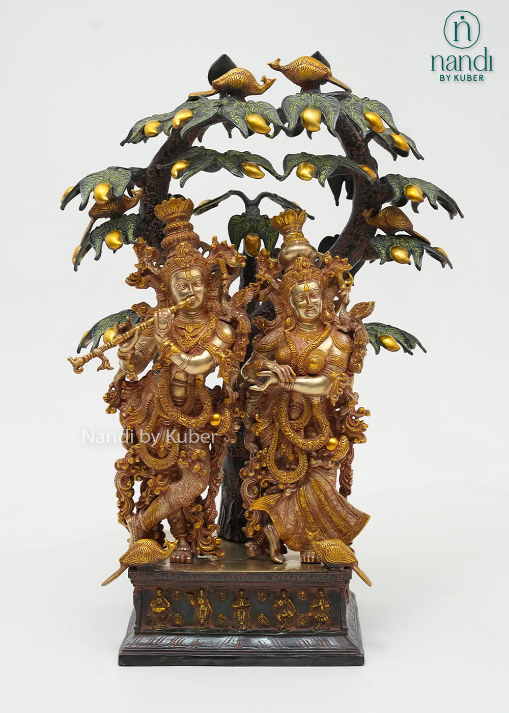 Decorative brass Radha Krishna sculpture beneath an intricately detailed tree with birds, symbolizing love, devotion, and harmony.