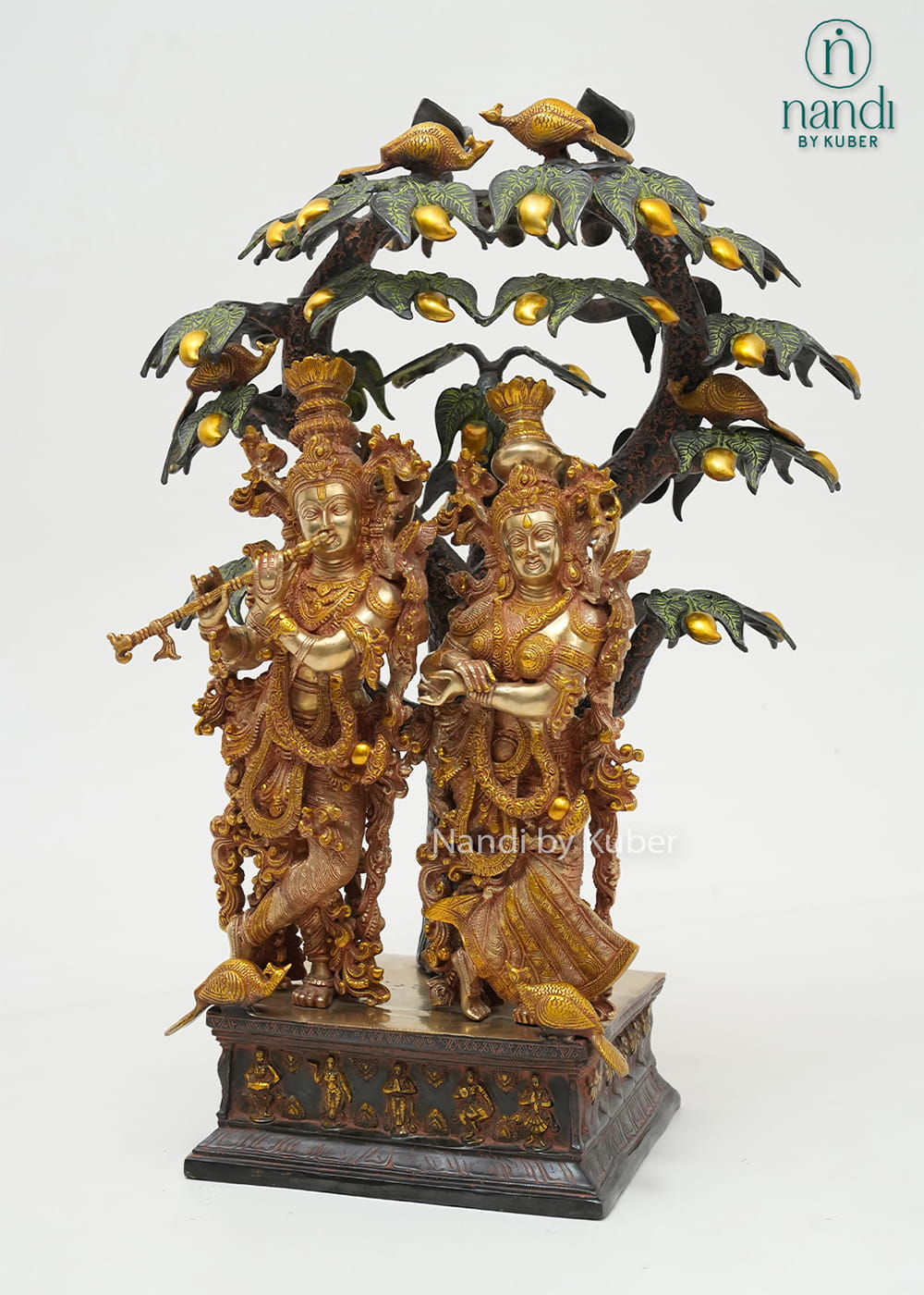 Decorative brass Radha Krishna sculpture beneath an intricately detailed tree with birds, symbolizing love, devotion, and harmony.