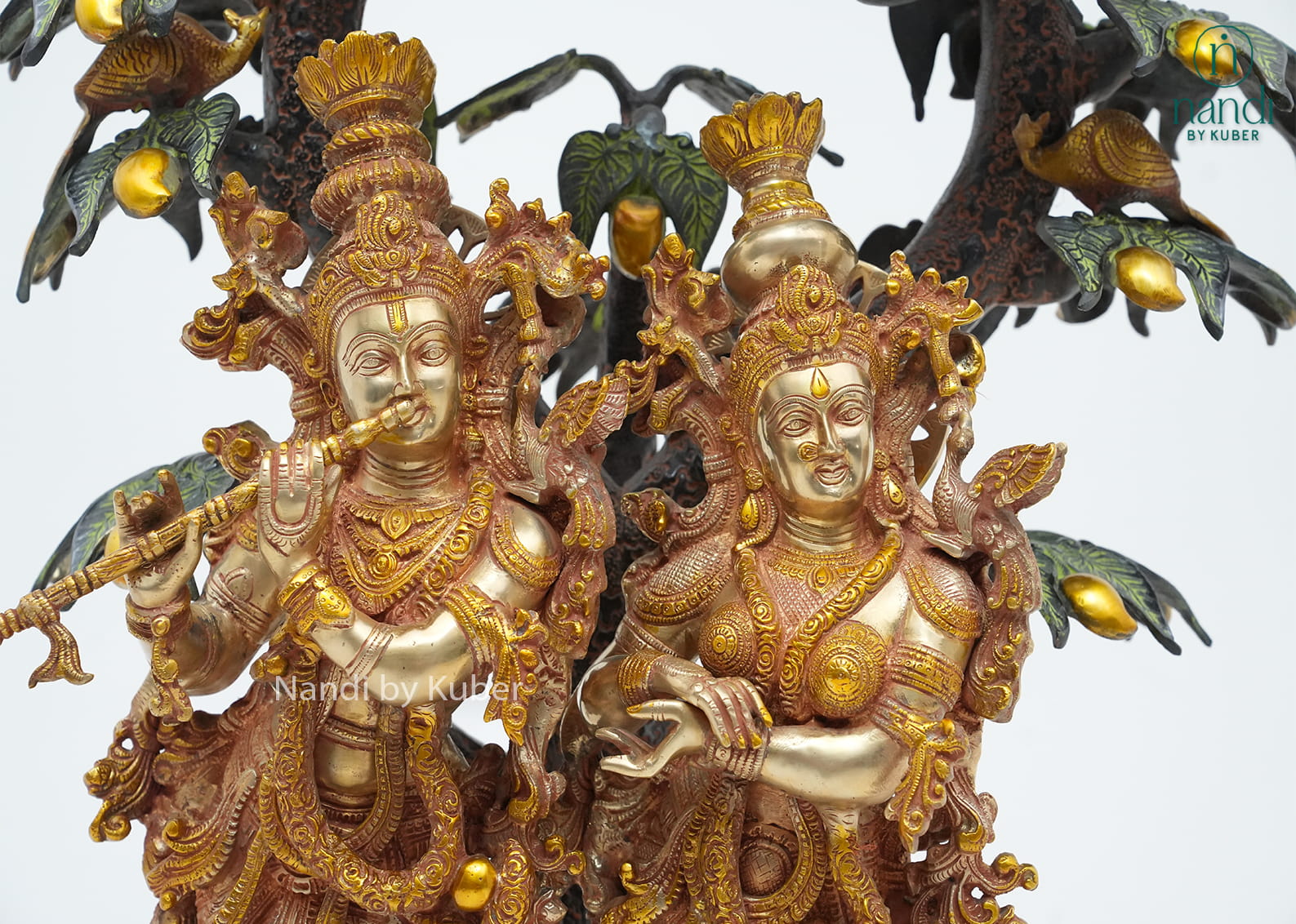 Decorative brass Radha Krishna sculpture beneath an intricately detailed tree with birds, symbolizing love, devotion, and harmony.