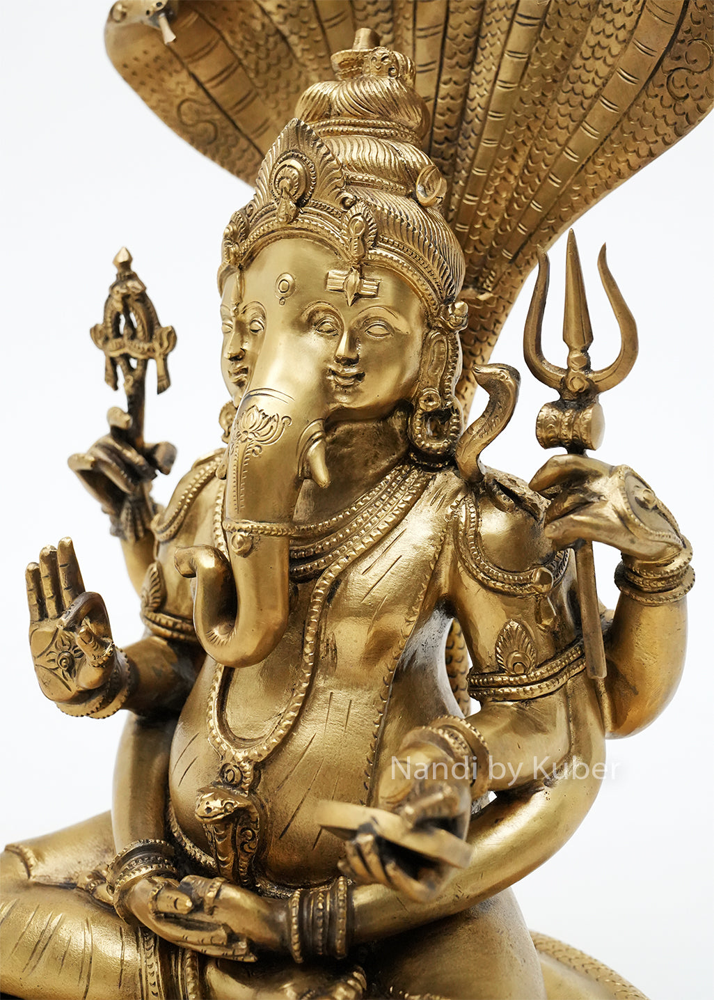 Handcrafted bronze Trimurti Ganesha idol with serpent hood canopy, intricate Hindu symbolism, and detailed pedestal base, ideal for home temples, spiritual décor, devotional worship, and religious gifting.
