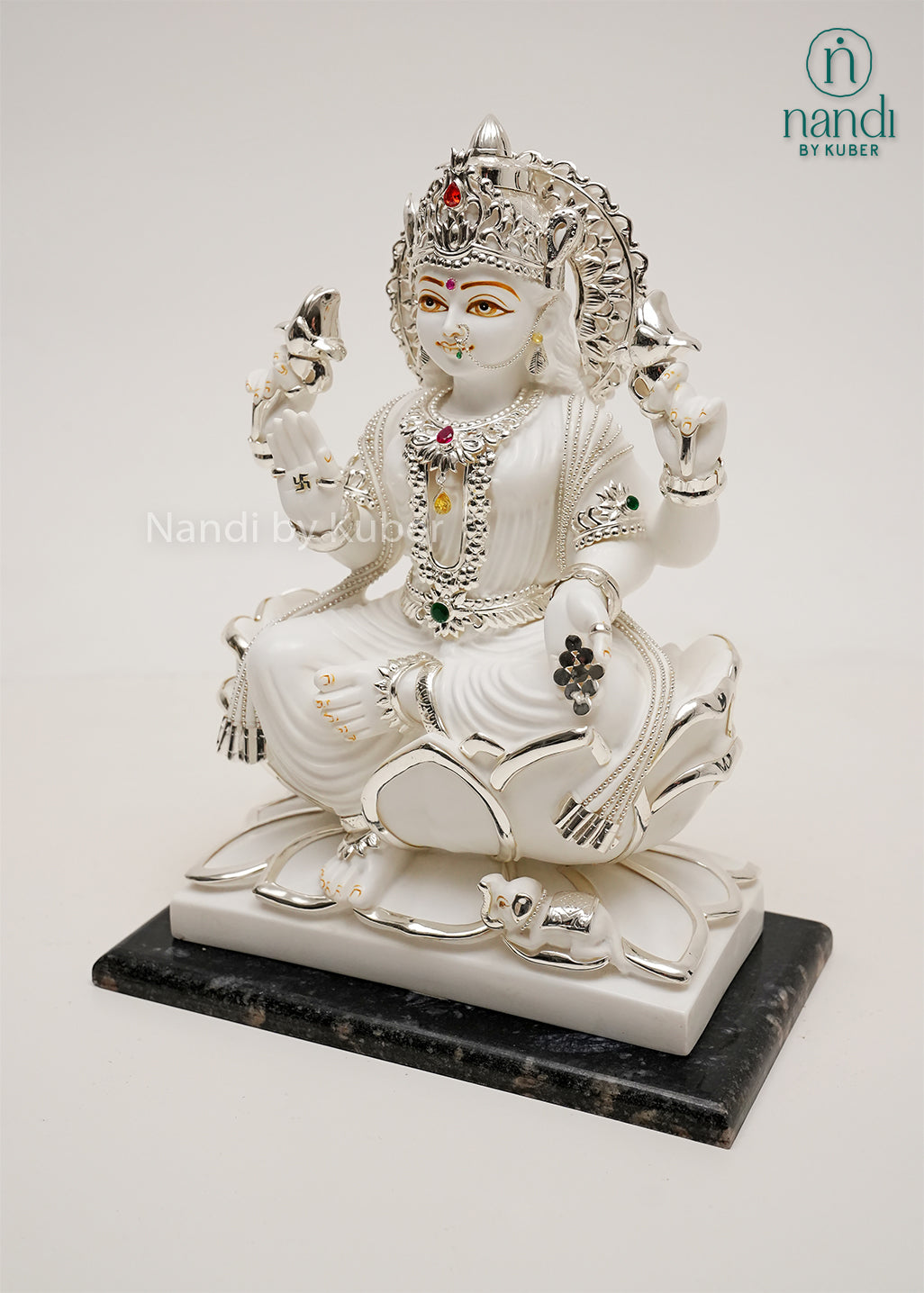White marble-style Lakshmi sitting on lotus statue with silver detailing, gemstone embellishments, and black base, ideal for home temples, spiritual décor, and prosperity-focused interiors.