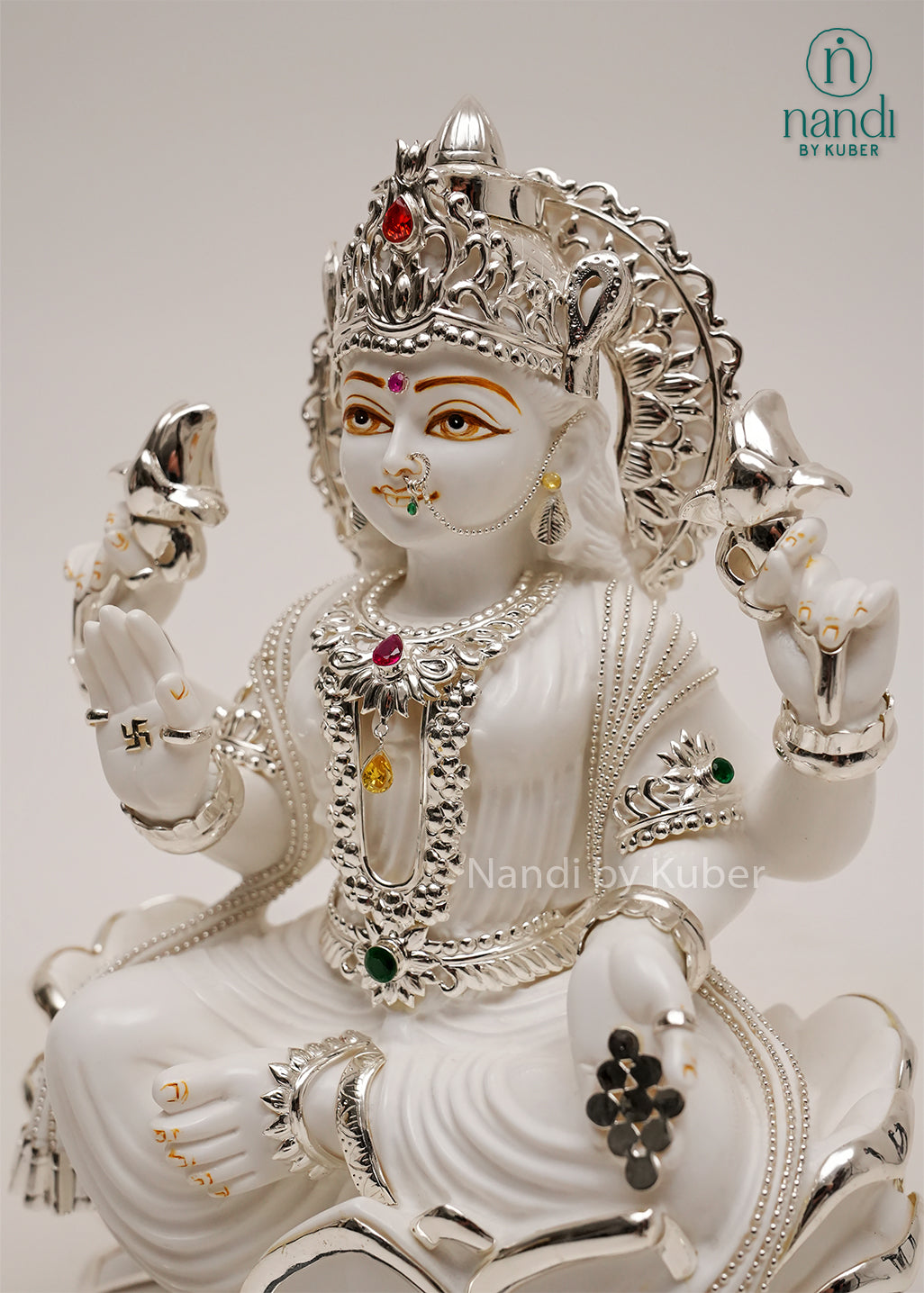 White marble-style Lakshmi sitting on lotus statue with silver detailing, gemstone embellishments, and black base, ideal for home temples, spiritual décor, and prosperity-focused interiors.