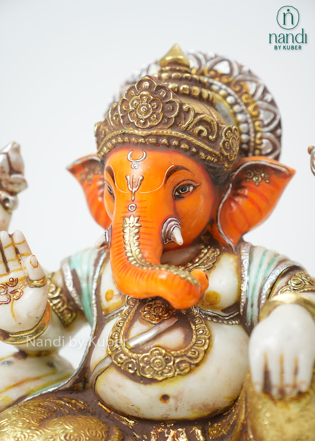 White marble-style Lord Ganesha statue with orange accents, antique gold detailing, ornate crown, and decorative pedestal base.
