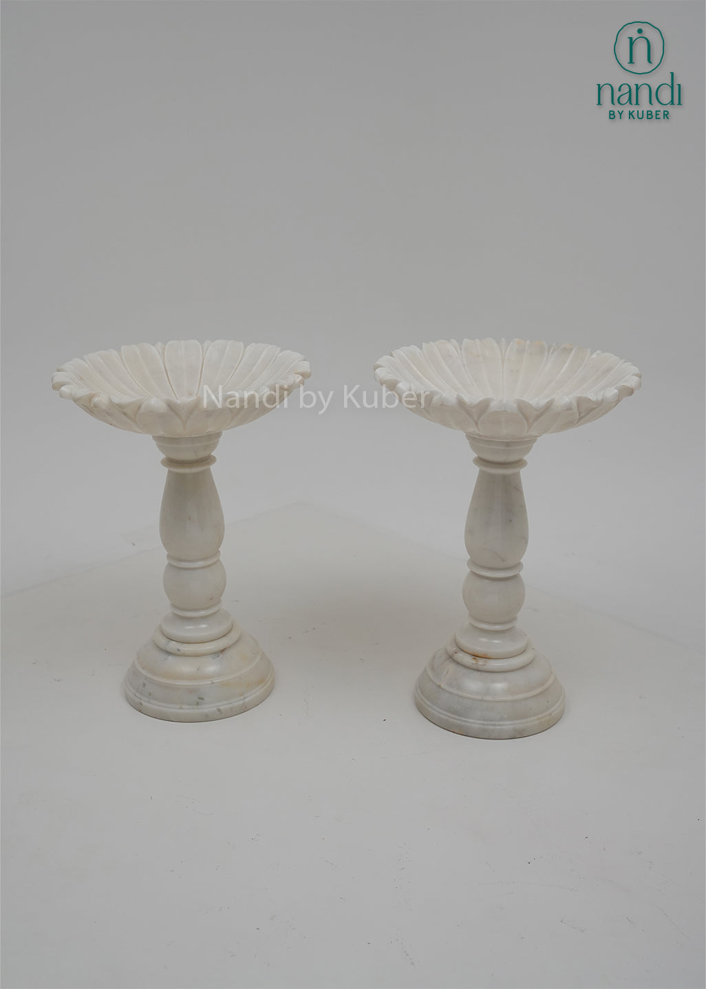 Set of two white marble urli bowls with pedestal stands and floral edges, decorative centerpiece bowls for home décor, festive decoration, weddings, and pooja arrangements.