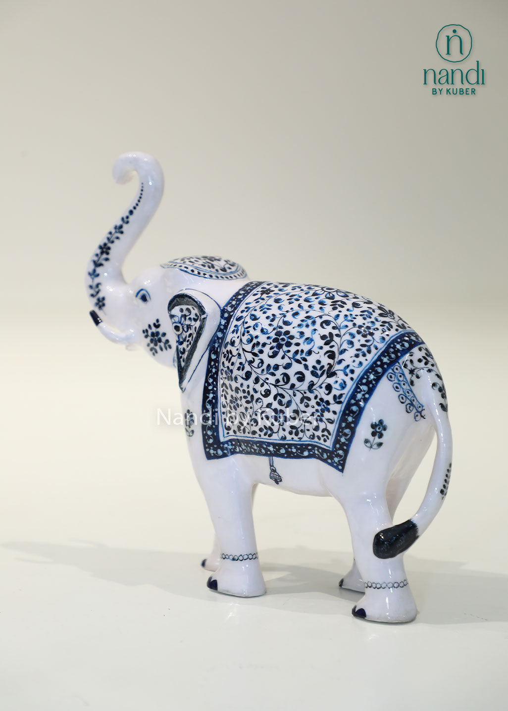 Handcrafted decorative elephant statue with raised trunk, white enamel finish and blue floral artwork, metal elephant figurine for home décor, office décor, and gifting.