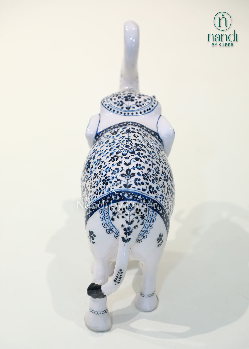 Handcrafted decorative elephant statue with raised trunk, white enamel finish and blue floral artwork, metal elephant figurine for home décor, office décor, and gifting.
