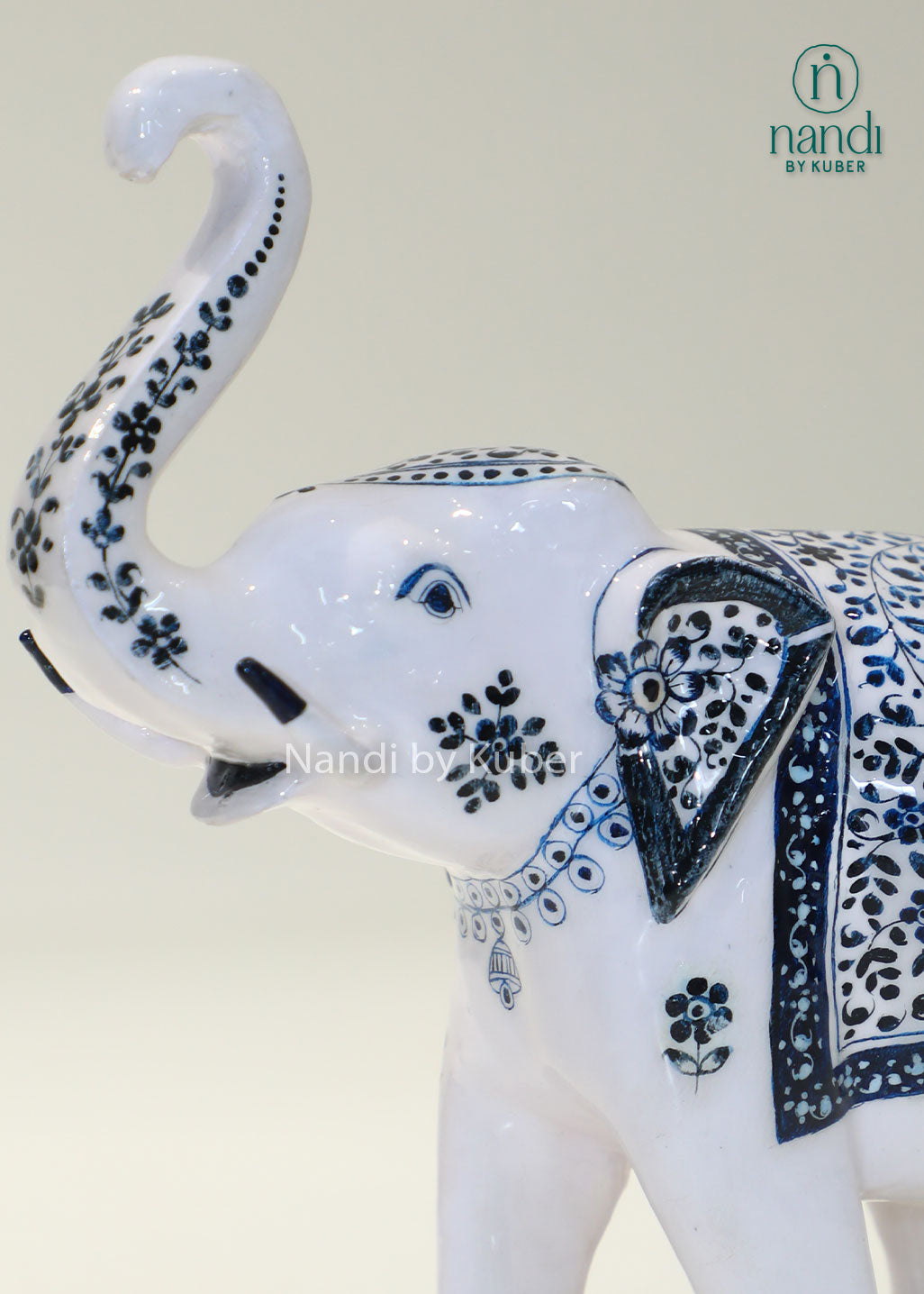 Handcrafted decorative elephant statue with raised trunk, white enamel finish and blue floral artwork, metal elephant figurine for home décor, office décor, and gifting.