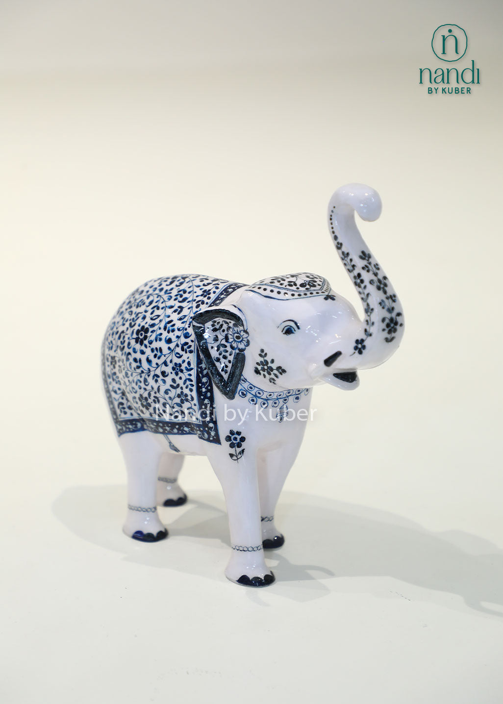 Handcrafted decorative elephant statue with raised trunk, white enamel finish and blue floral artwork, metal elephant figurine for home décor, office décor, and gifting.