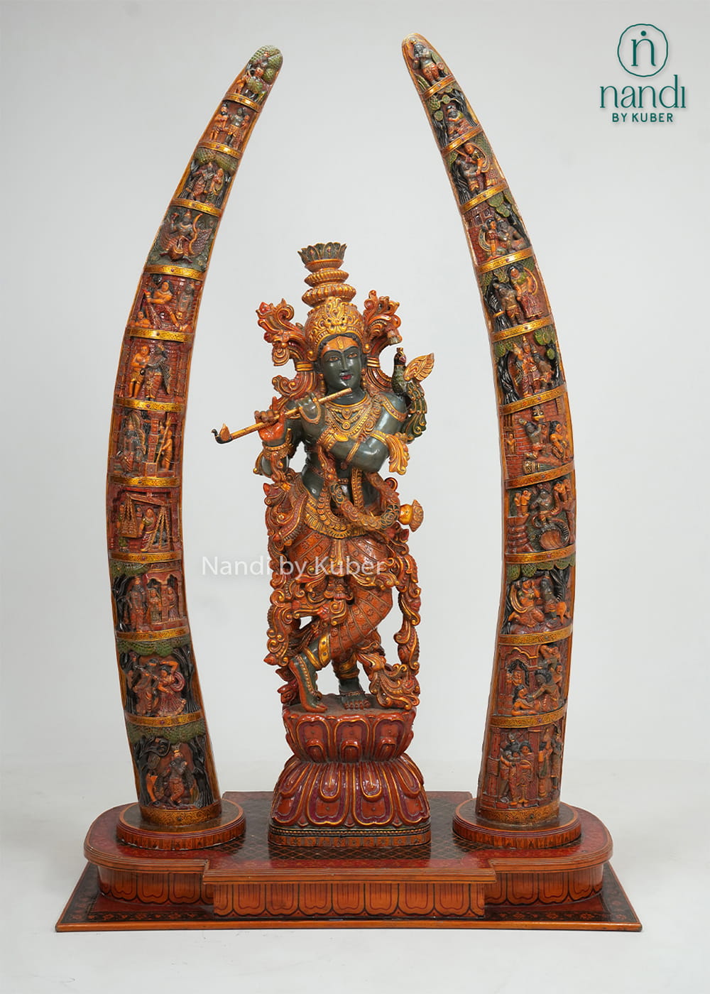 Decorative wooden Lord Krishna statue playing the flute, framed by two intricately carved tusk-style arches with detailed craftsmanship 