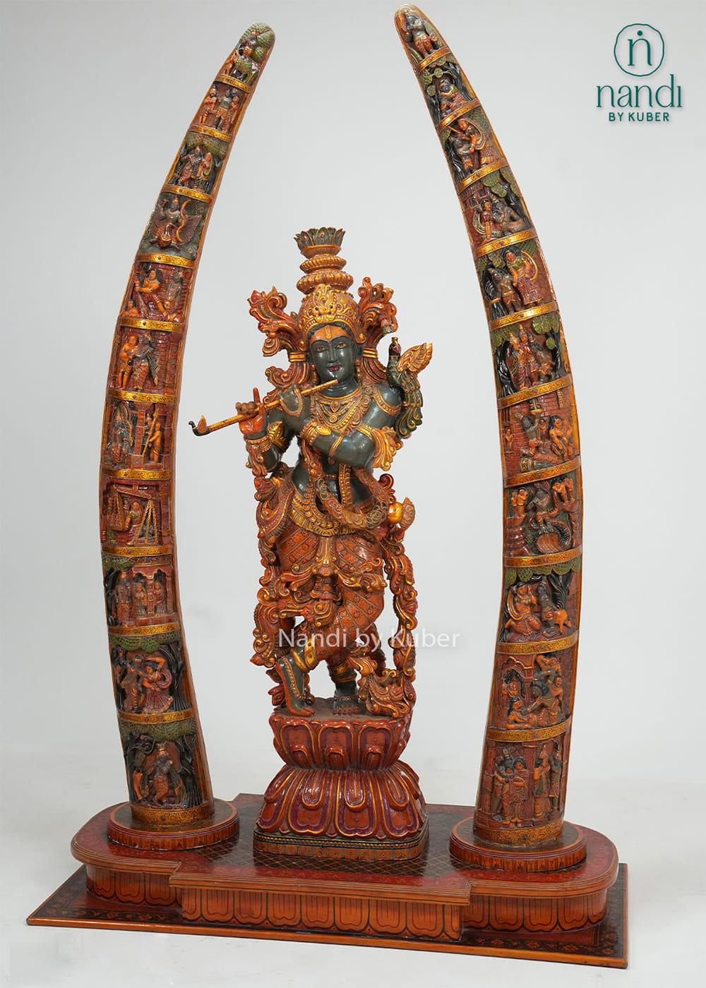 Decorative wooden Lord Krishna statue playing the flute, framed by two intricately carved tusk-style arches with detailed craftsmanship